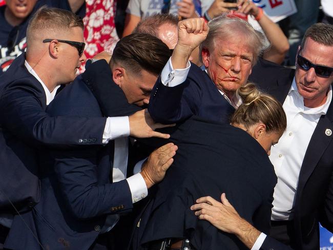 US Republican candidate Donald Trump is seen with blood on his face surrounded by secret service agents as he is taken off the stage at a campaign event at Butler Farm Show Inc. in Butler, Pennsylvania, on July 13, 2024. Trump was hit in the ear in an apparent assassination attempt by a gunman at a campaign rally on Saturday, in a chaotic and shocking incident that will fuel fears of instability ahead of the 2024 US presidential election. The 78-year-old former president was rushed off stage with blood smeared across his face after the shooting in Butler, Pennsylvania, while the gunman and a bystander were killed and two spectators critically injured. (Photo by Rebecca DROKE / AFP) / QUALITY REPEAT