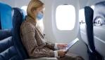 Portrait of young beautiful woman with long blond hair wearing mask inside airplane while reading safety instructions.