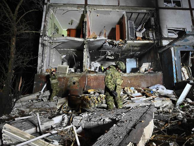 A Ukrainian law enforcement officer stands among rubbles next to a damaged residential building following a drone attack in Kharkiv late on December 20, 2024. (Photo by SERGEY BOBOK / AFP)