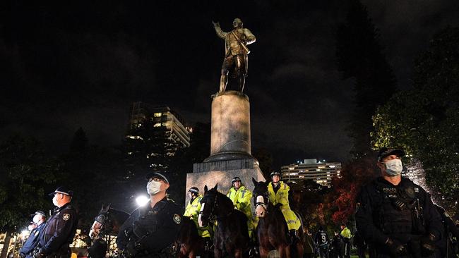 Police stand guard at the statue of Captain Cook in Hyde Park on Friday night during an anti-racism protest. The statue has since been defaced.