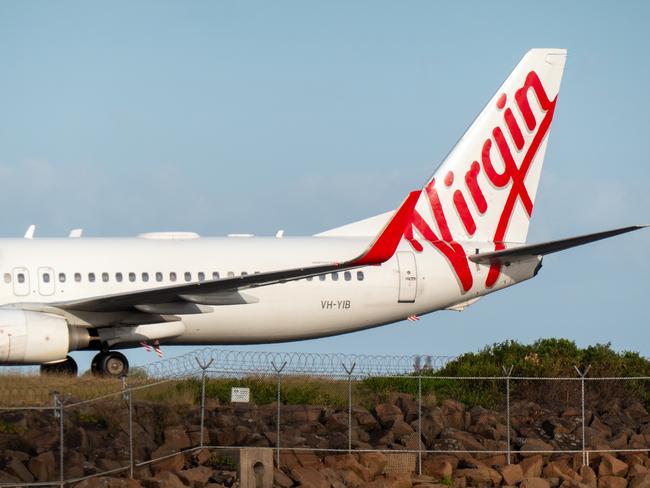 A Virgin Australia Boeing B737-8FE plane, registration VH-YIB, taxiing to the international terminal after landing at Sydney Kingsford Smith Airport as flight VA182 from Nadi. In the foreground is the airport's security fence. This image was taken from Kyeemagh Beach, Botany Bay on a sunny and partly cloudy afternoon on 31 December 2024.