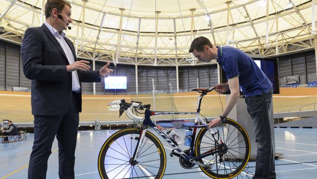 International Cycling Union (UCI) technical manager Mark Barfield (L) gestures next to a staff member holding a tablet to scan a bicycle.