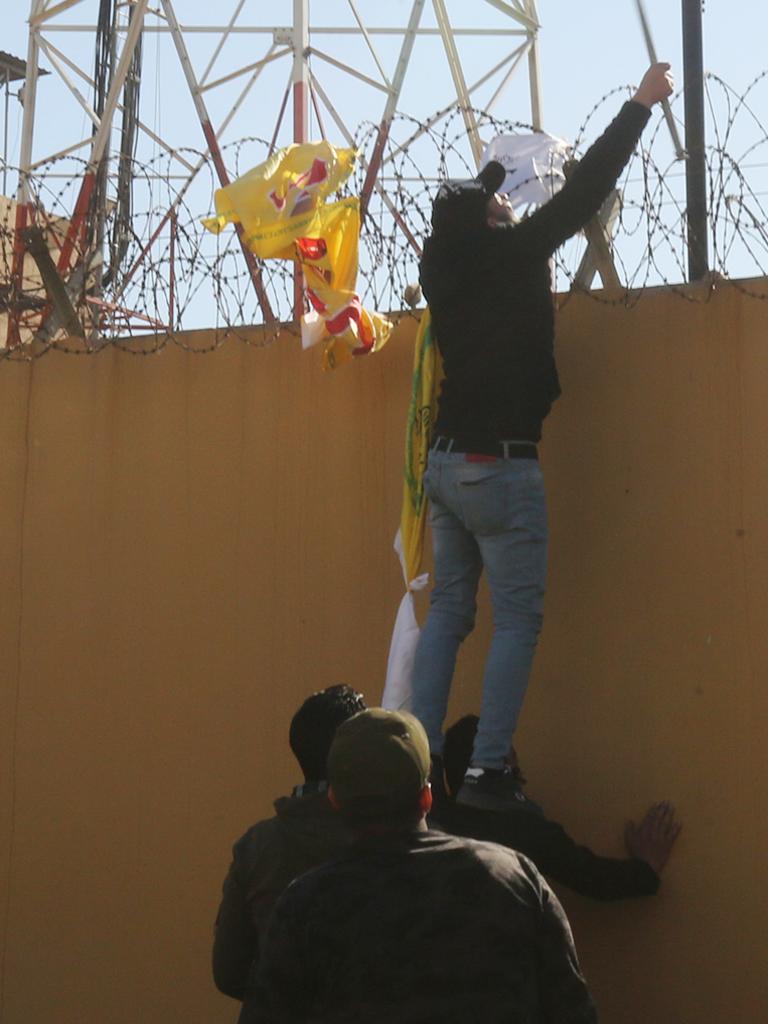 Iraqi protesters try to disable the camera on the outer wall of the US embassy in Baghdad's Green Zone during an angry demonstration. Picture: AFP