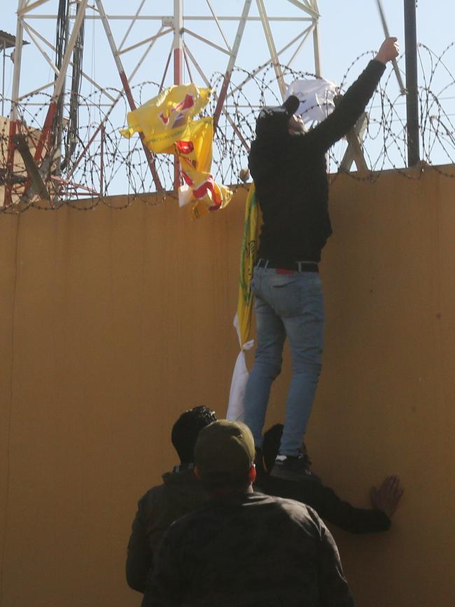 Iraqi protesters try to disable the camera on the outer wall of the US embassy in Baghdad's Green Zone during an angry demonstration. Picture: AFP