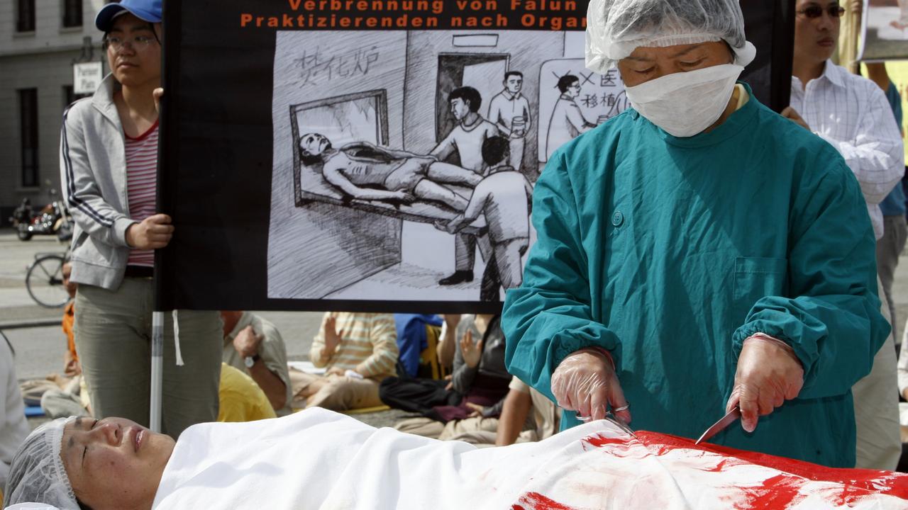 A protester dressed as a Chinese doctor simulates removing organs from another dressed as a Falun Gong practitioner at a protest in Berlin. Picture: Getty Images