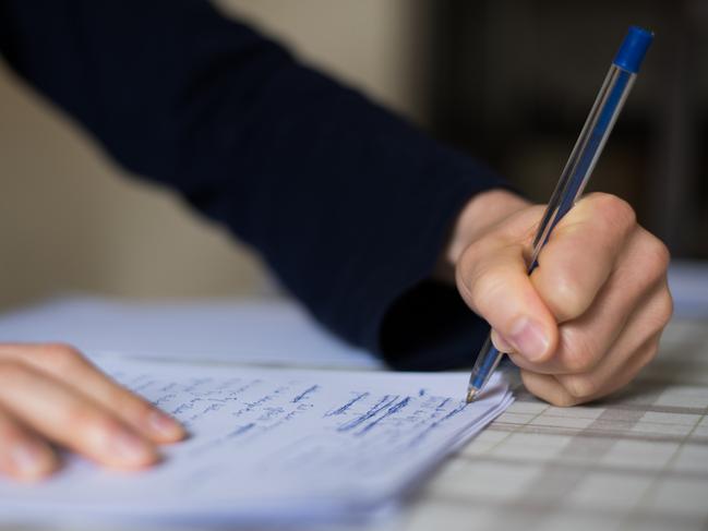 The photo is taken indoors with copy space. A woman in side view is writing words of a speech on white paper.