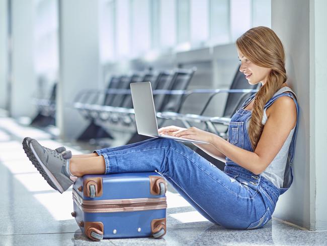 Shot of a young woman using a laptop while sitting on the floor in an airport