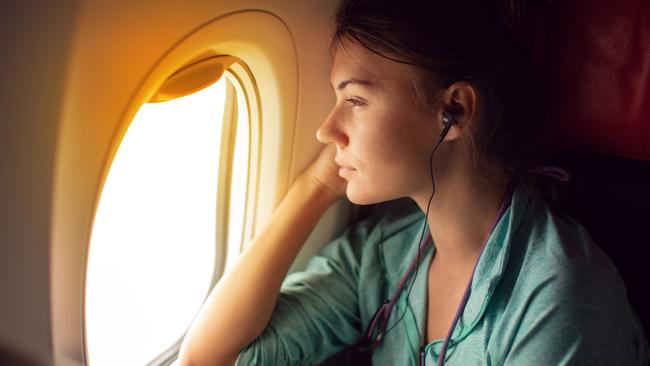 ESCAPE:  Young woman sitting in the plane, looking away through the window and listeting music with headphones  Picture: Istock