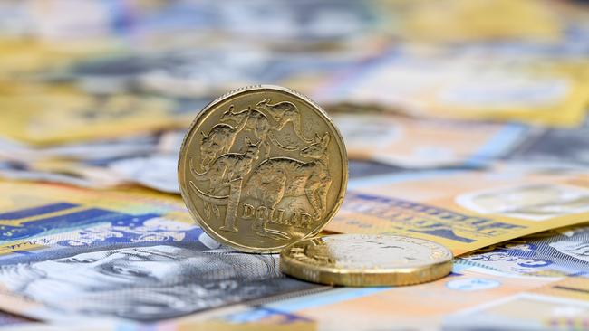 A single Australian One Dollar coin standing on its edge on top of Australian fifty dollar bills; saving money generic