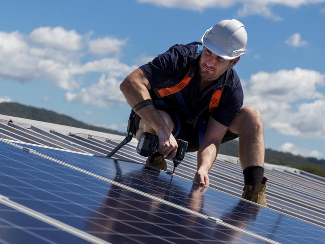 TRADESMAN/ TRADIE/BUILDING INDUSTRY:  Solar panel installer with drill installing solar panels on roof on a sunny day