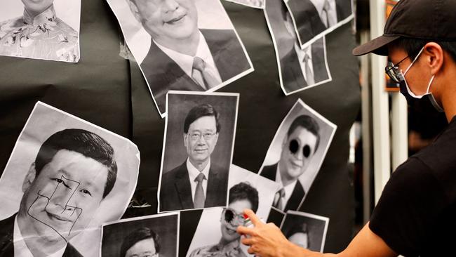 An activist sprays paint on portraits depicting China's President Xi Jinping, Hong Kong's Chief Executive Carrie Lam and Hong Kong's Chief Executive-elect John Lee. Picture: AFP