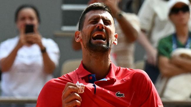 Serbia's Novak Djokovic celebrates holding his country's badge after beating Spain's Carlos Alcaraz in their men's singles final tennis match on Court Philippe-Chatrier at the Roland-Garros Stadium during the Paris 2024 Olympic Games, in Paris on August 4, 2024. (Photo by Patricia DE MELO MOREIRA / AFP)