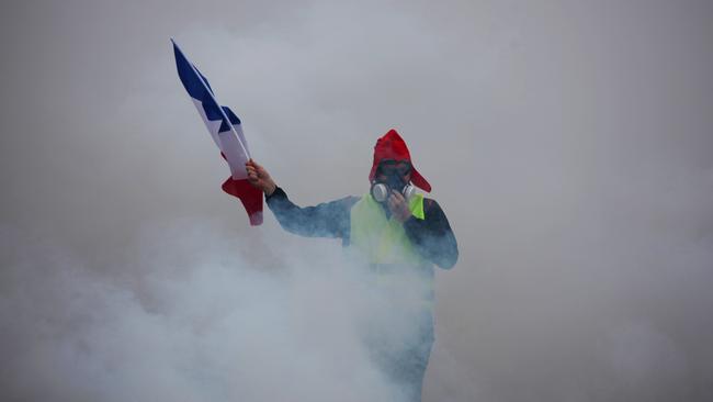 A demonstrator holds a French flag as he walks amid the tear gas. Picture: AFP