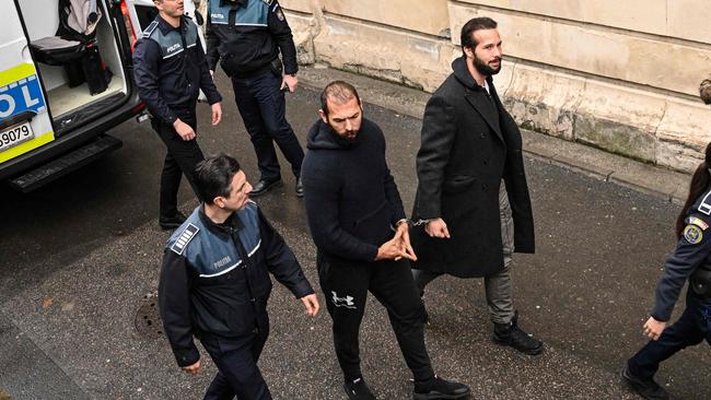 Andrew Tate went out of his way to make the symbol with his hands despite being handcuffed to his brother, Tristan. Picture: Daniel Mihailescu/AFP