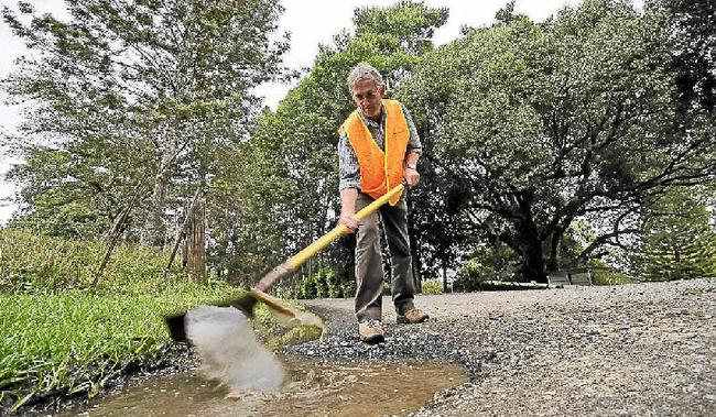 DIGGING IN: Councillor David Yarnall shovelling water from a 10cm deep pothole on Keerong Rd at The Channon. He has suggested giving residents the equipment to fix roads themselves to speed up the rate of repairs. Doug Eaton