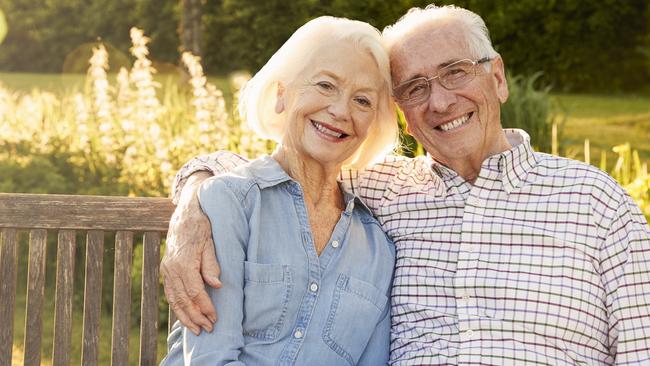 Senior Couple Sitting On Garden Bench In Evening Sunlight;  Happy retirees retirement generic.