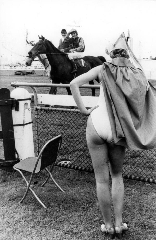 A jockey waves to a spectator dressed in a swim suit and cape in 1978.