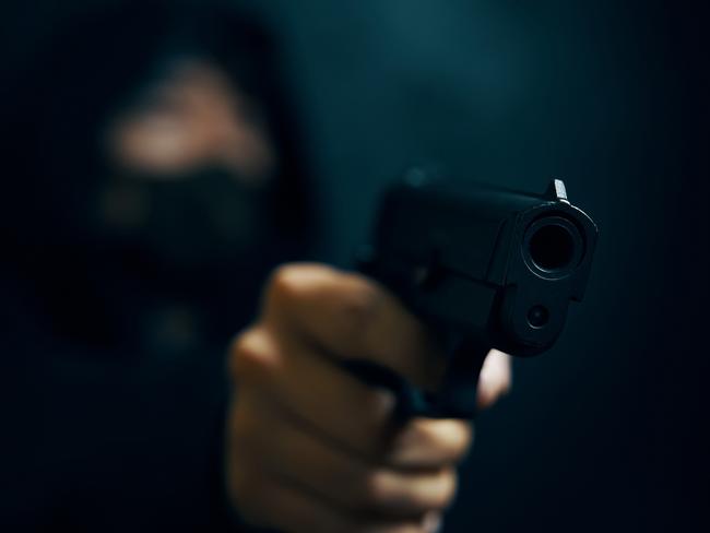 Man in hood threatens with firearm. Masked robber with gun. Weapon in person's hands. Murderer or armed thief. Criminal with pistol. Generic image. Picture: Savusia Konstantin