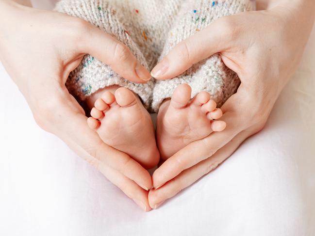 Baby feet in mother hands. Tiny Newborn Baby's feet on female Heart Shaped hands closeup. Mom and her Child. Happy Family concept. Beautiful conceptual image of Maternity