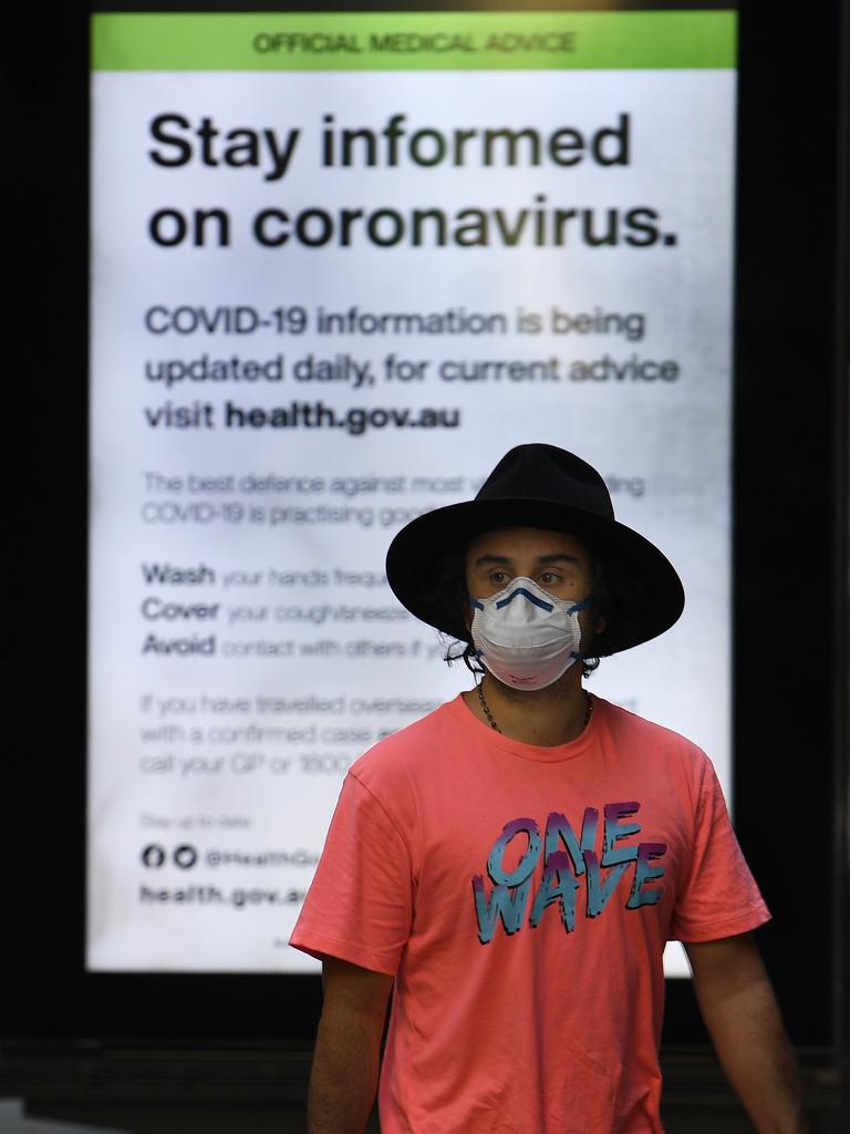 A man wearing a protective mask walks past an official medical advice advertisement in Sydney. Picture: AAP