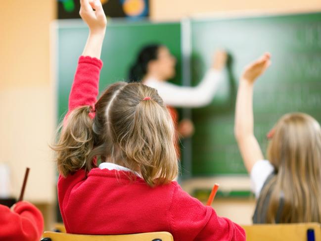 Elementary school kids raising their hands in class to answer a teacher's question.