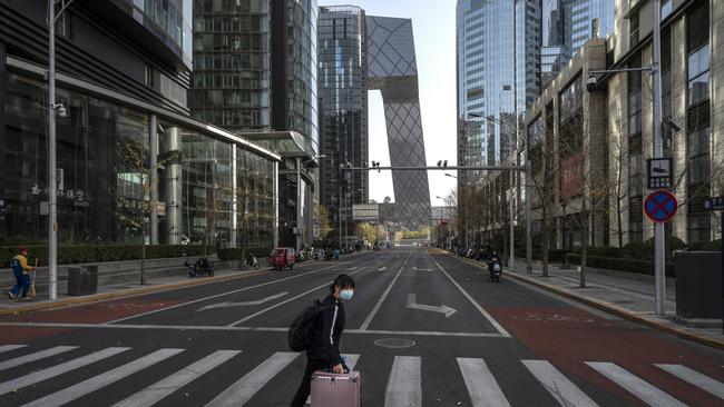 A woman walks across a nearly empty street with her luggage in the Central Business District of Beijin on November 25.