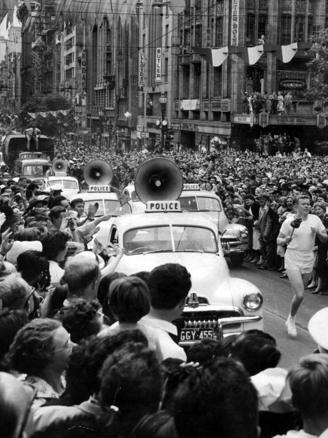 1956: Police escort the Olympic torch as a runner carries it along Collins Street, Melbourne.