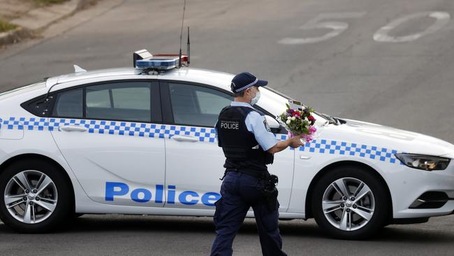 A police officer brings flowers to a home in Pendle Hill where a woman in her 80s has died from Covid-19. Picture: Jonathan Ng