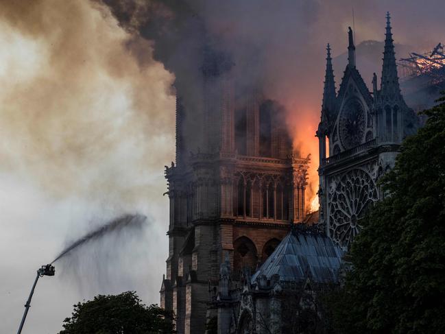 Firefighters douse flames billowing from the roof at Notre-Dame Cathedral in Paris on April 15, 2019. - A huge fire swept through the roof of the famed Notre-Dame Cathedral in central Paris on April 15, 2019, sending flames and huge clouds of grey smoke billowing into the sky. The flames and smoke plumed from the spire and roof of the gothic cathedral, visited by millions of people a year. A spokesman for the cathedral told AFP that the wooden structure supporting the roof was being gutted by the blaze. (Photo by THOMAS SAMSON / AFP)