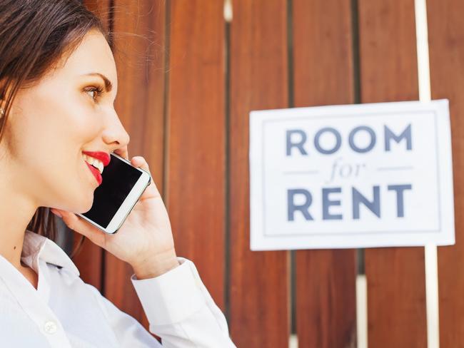 caucasian woman in white shirt standing in front of wooden fencing with "room for rent" ads and calling to house owner