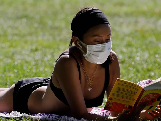 A woman wears a facemask as she reads a book in the sunshine in London Fields, north east London on May 20, 2020, as temperatures in the capital are expected to reach 28C (82.4F). - British Prime Minister Boris Johnson said Wednesday the country will have 25,000 virus tracing staff recruited by June so the country can 