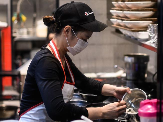 A woman seen wearing a protective face mask in a restaurant kitchen in Sydney, Monday, March 16, 2020. (AAP Image/James Gourley) NO ARCHIVING