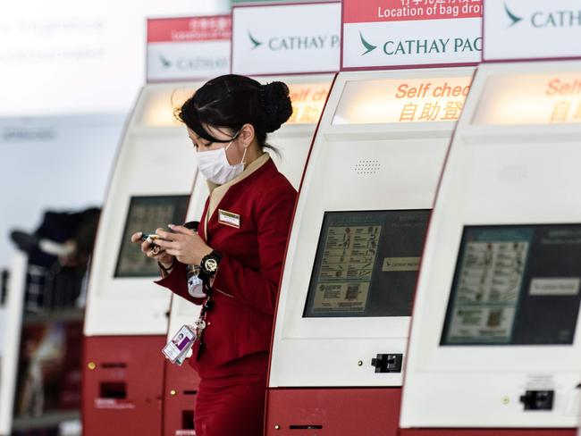 A mask-clad Cathay Pacific employee walks past a row of self check-in counters in Hong Kong. Picture: AFP