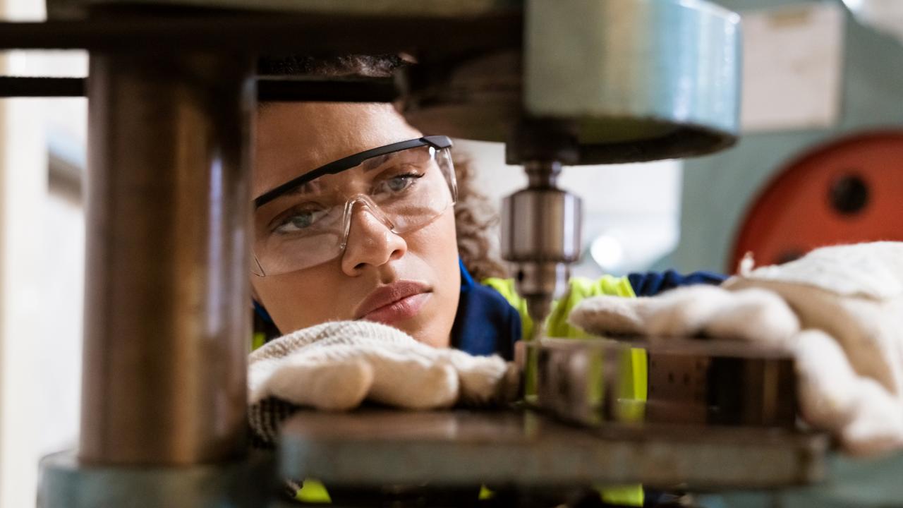 TRADESWOMAN/ TRADE WOMAN/ TRADESMAN/ TRADIE/BUILDING INDUSTRY: Close-up of female apprentice using yoke machine. Female engineer is wearing protective glasses in factory. She is working in manufacturing industry.