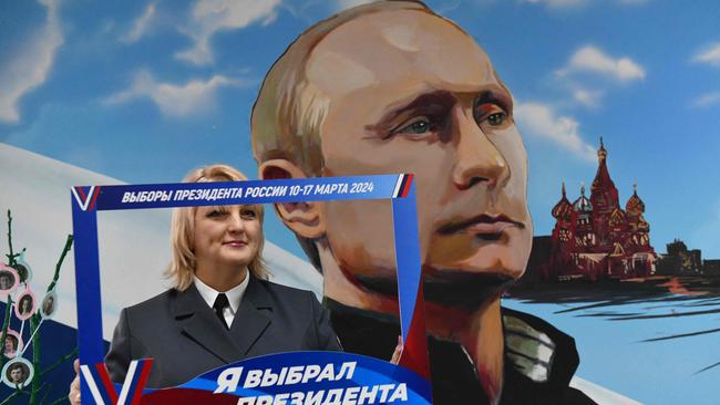 A woman poses with a frame reading ‘I chose a president’ in front of a mural depicting Vladimir Putin during Russia's presidential election. Picture: AFP.