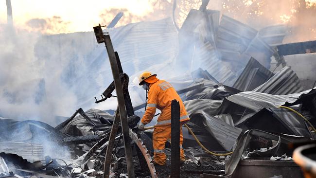 A fireman hoses down the remains of three houses that have been destroyed by fire on the Noosa North Shore. Picture: AAP/Darren England