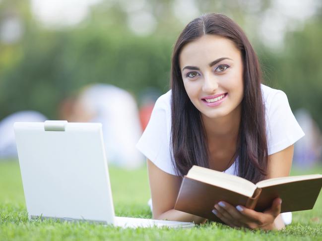 Brunette girl with notebook and book on green grass in the park. To illustrate online study. iStock image