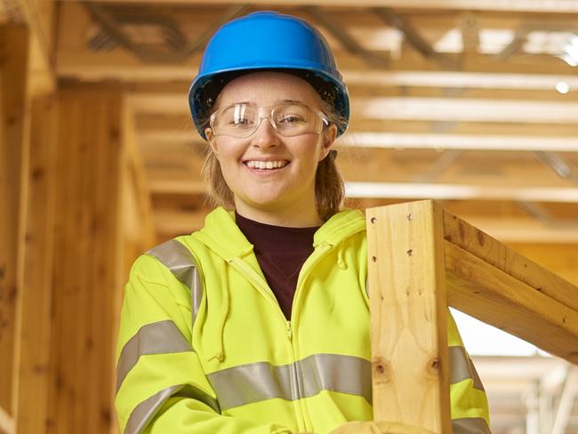 a female construction worker carries some studwork on a building site housing development and is assited by a male colleague .