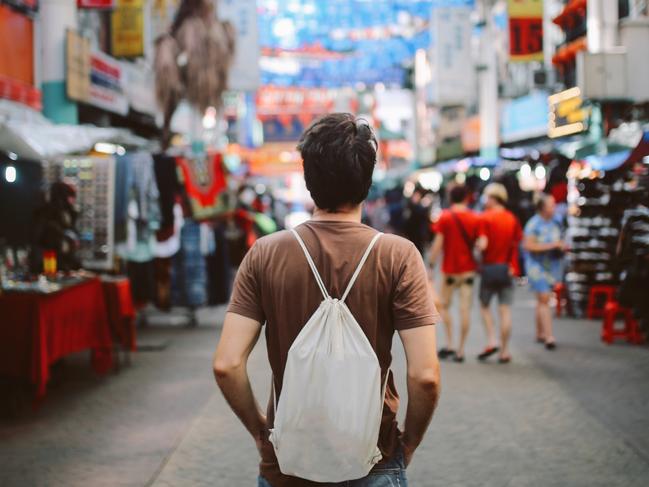 Rear view image of a young man, solo traveler, walking in the Chinatown district of Kuala Lumpur, Malaysia. He is wearing a white rucksack, enjoying walking and shopping in Malaysia capital.