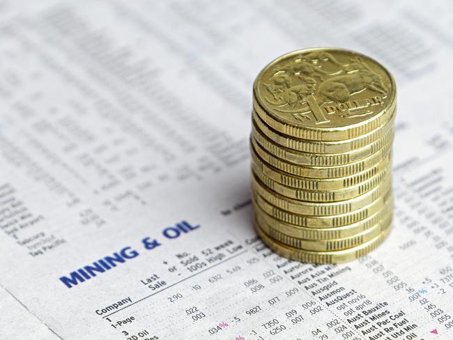 Eleven Australian one dollar coins stacked on a newspaper reporting share market prices for Mining and Oil. generic investing