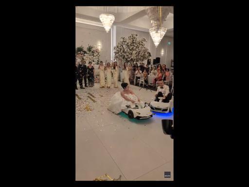 Bride and groom drift into wedding reception in electric toy cars