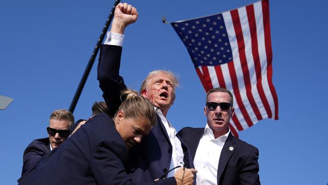 Donald Trump raises a defiant fist despite Secret Service personnel attempts to shield the then Republican candidate. Picture: AP