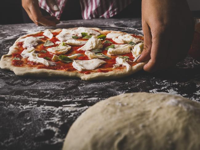 A closeup of a womans hands making an Italian pizza on a floured surface from istock