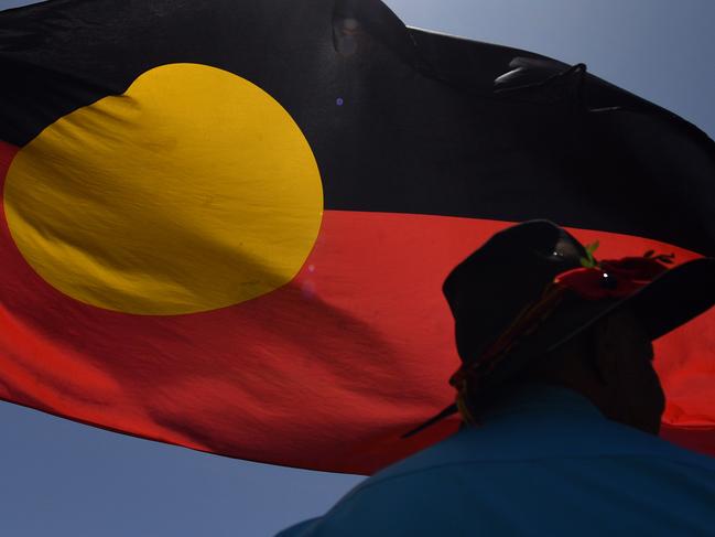 A man is seen under the indigenous flag protesting Aboriginal rights on Australia Day at Parliament House in Canberra, Sunday, January 26, 2020. (AAP Image/Mick Tsikas) NO ARCHIVING