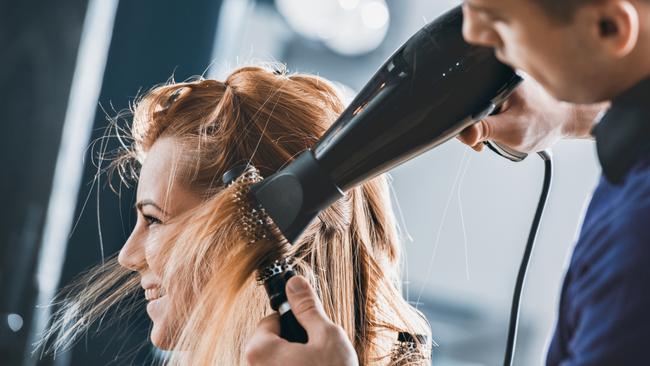 Young hairdresser drying customers hair with round brush at hair salon.