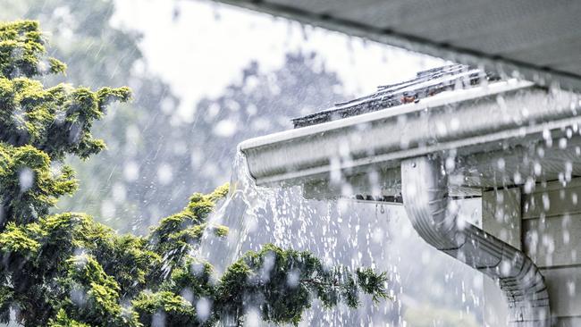 Drenching downpour rain storm water is overflowing off the tile shingle roof - streaming, rushing and splashing out over the overhanging eaves trough aluminum roof gutter system on a suburban residential colonial style house near Rochester, New York State, USA during a torrential mid-summer July downpour.