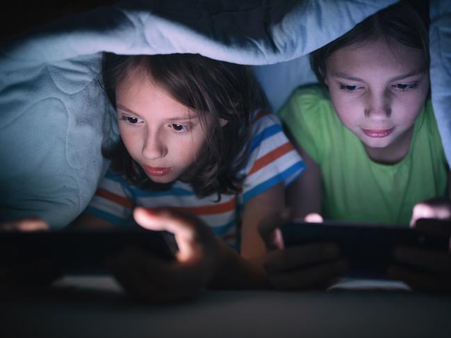 Boy and girl playing games on mobile phones while lying on bed in bedroom under the blanket. They are spending some nice time together that makes them happy.  - picture istock