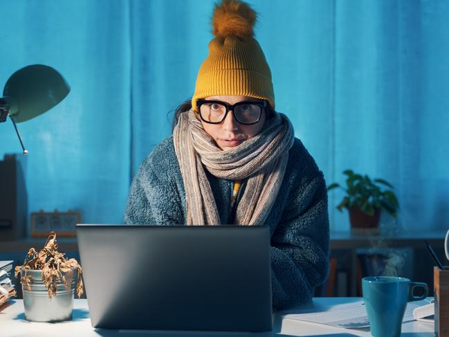 Woman sitting at desk and feeling cold, she is wearing warm clothes and saving money on her utility bills, electricity generic winter