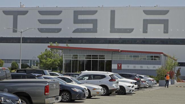 A masked man walks in a nearly full Tesla plant parking lot at Fremont on Monday, in an indication the company could be about to resume production. Picture: AP