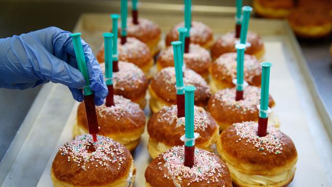 An employee puts syringes full of raspberry jelly on the top of a berliner (German doughnut) at the bakery Kreyenbuhl in Muri, Switzerland. Picture: AFP